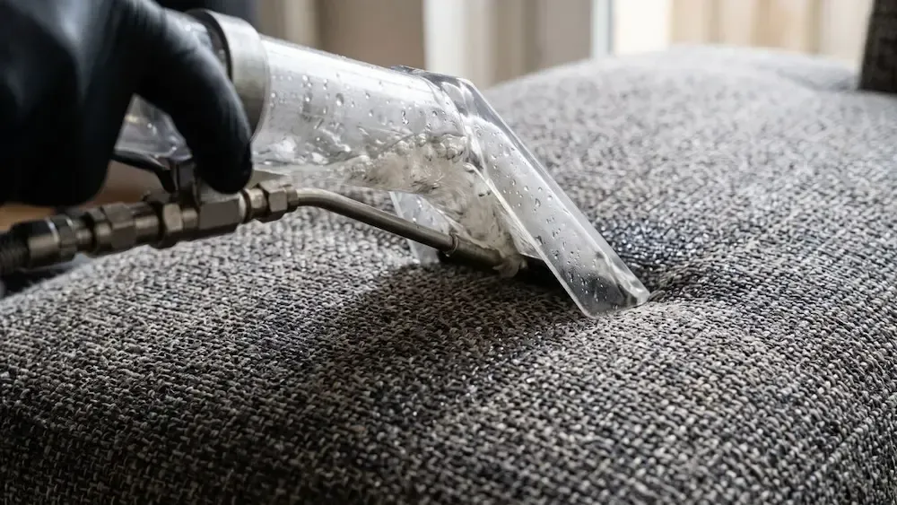 Steam cleaning a gray upholstered surface with a handheld nozzle