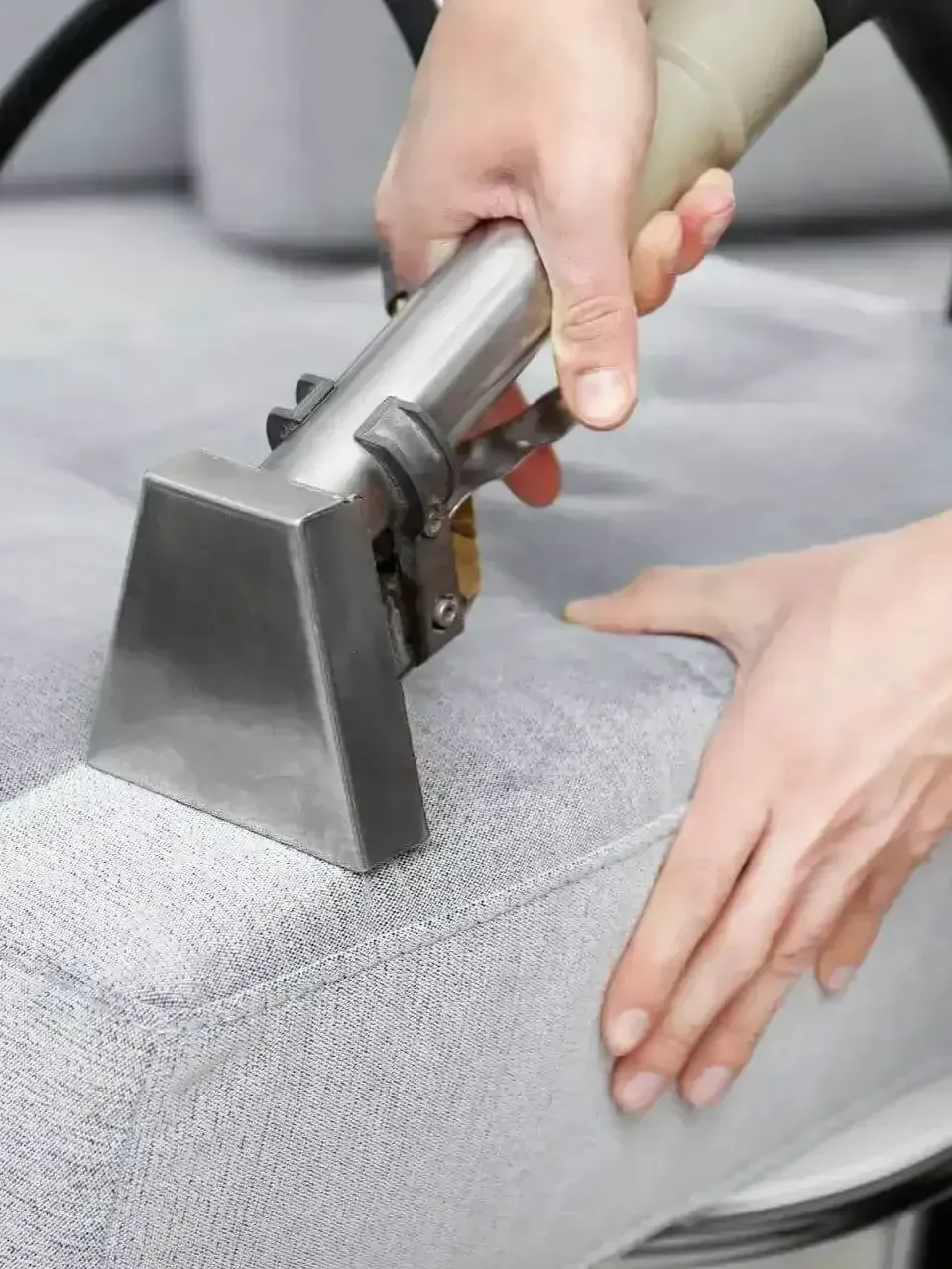 a person is cleaning a couch with a vacuum cleaner .