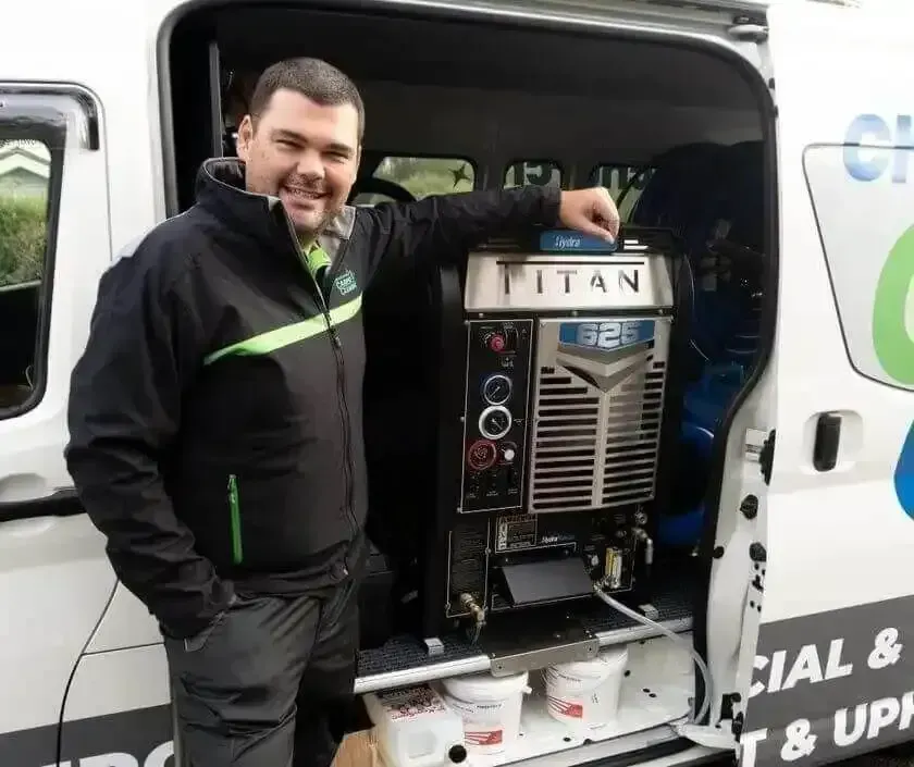 Man standing beside a TITAN machine in the open side of a white service van, smiling and pointing at it