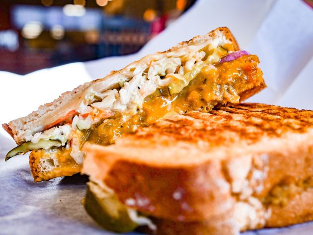 A grilled sandwich is cut in half on a piece of wax paper