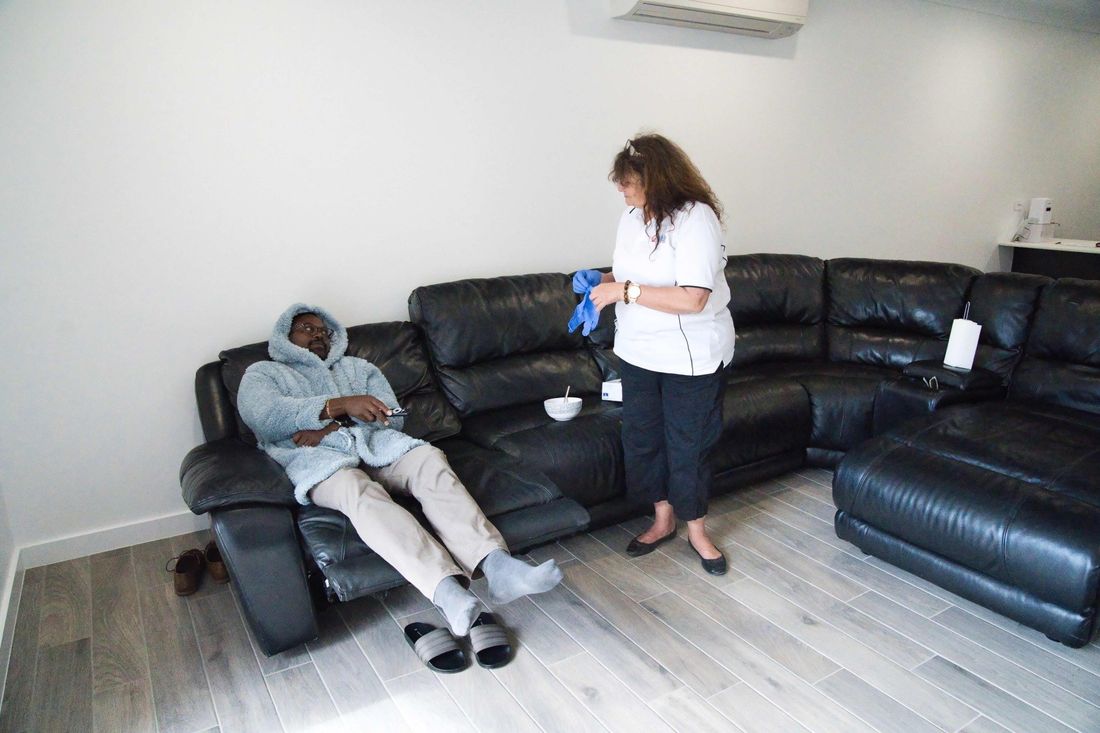 A woman is standing next to a man sitting on a couch in a living room.
