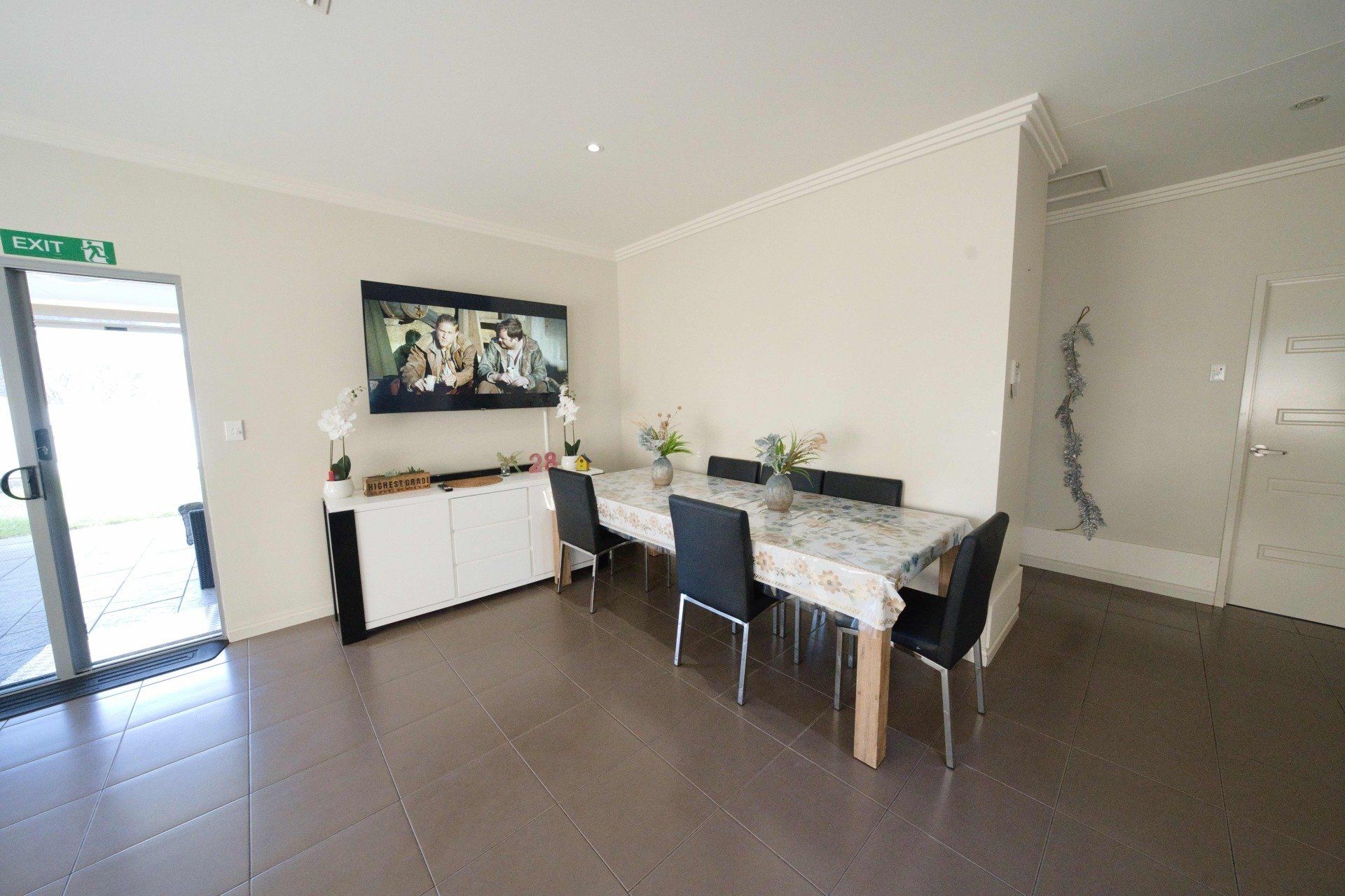 A dining room with a long table and chairs and a television on the wall.
