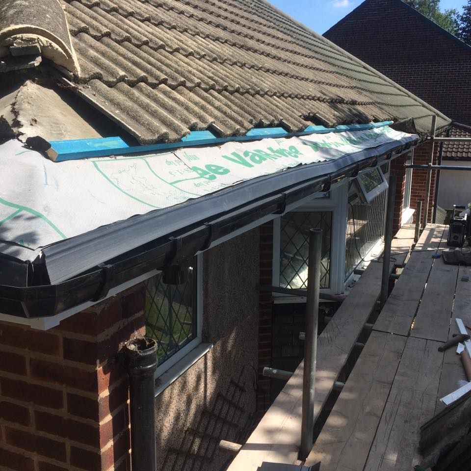 Roof repair on a house with white weatherproof membrane and blue tape along the eaves