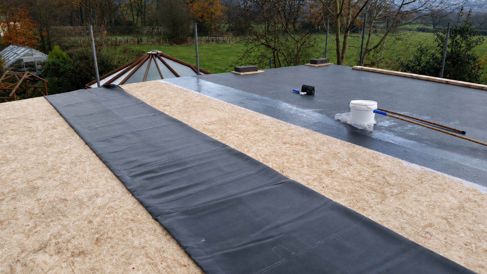 Flat rooftop with black waterproof membrane, white gravel, and a small vent under a cloudy sky.