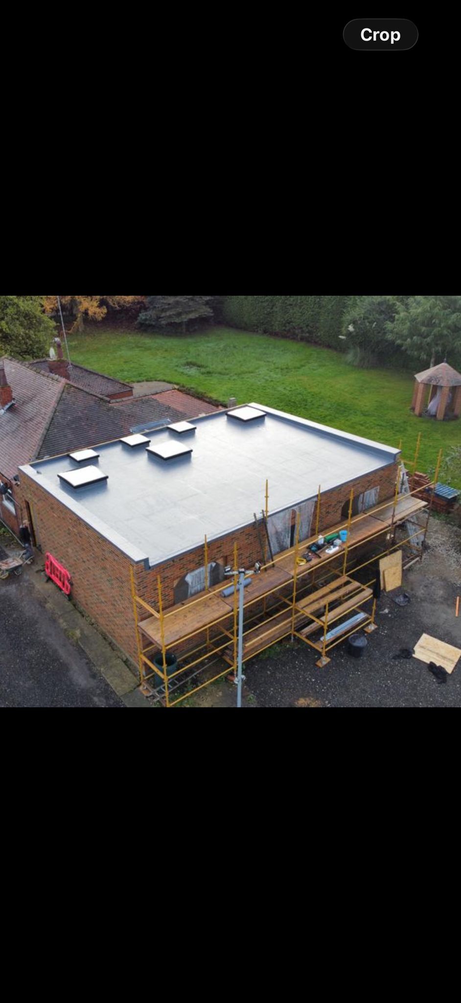 Aerial view of a house under construction with a white roof and wooden scaffolding around it.
