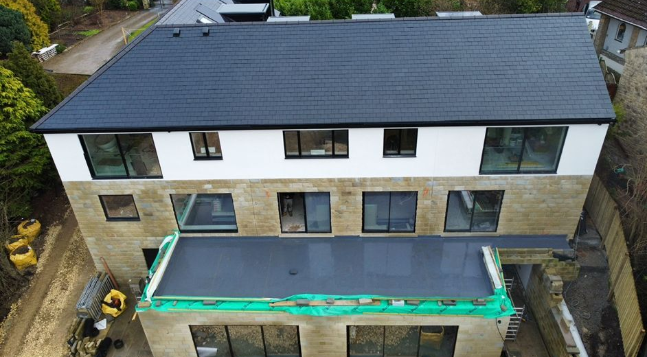 Aerial view of a modern two-story house with a dark roof and a terrace under construction.