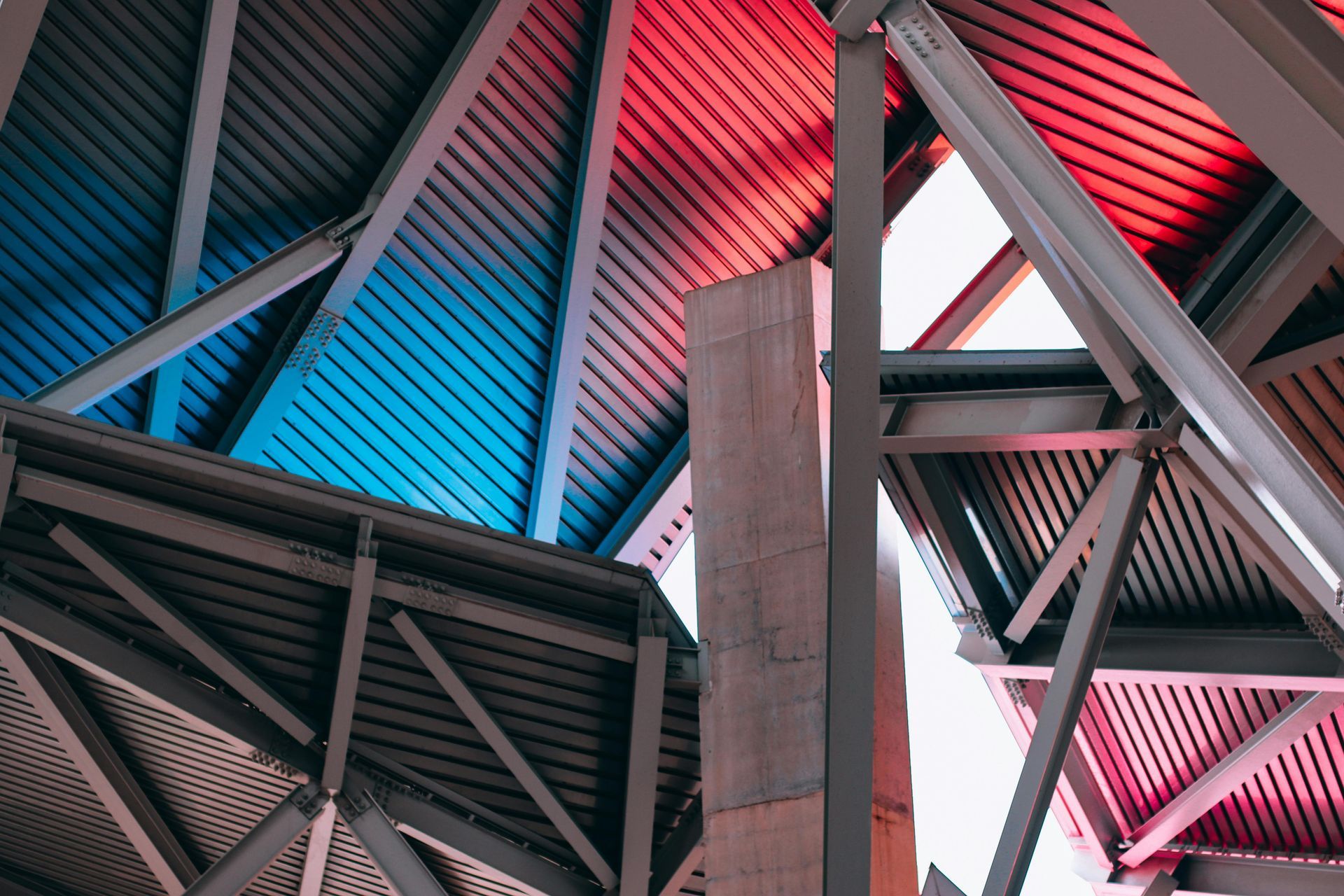 Abstract view of architectural steel beams and corrugated metal panels illuminated with blue and red light.