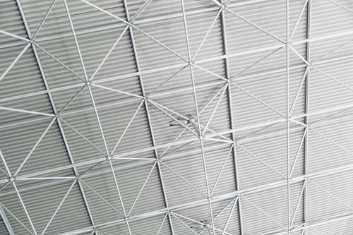 An industrial metal ceiling with a repeating pattern of white trusses and support beams against a corrugated roof.