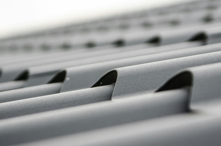 Close-up, angled view of textured, matte gray metal roof panels with overlapping, curved ridges.