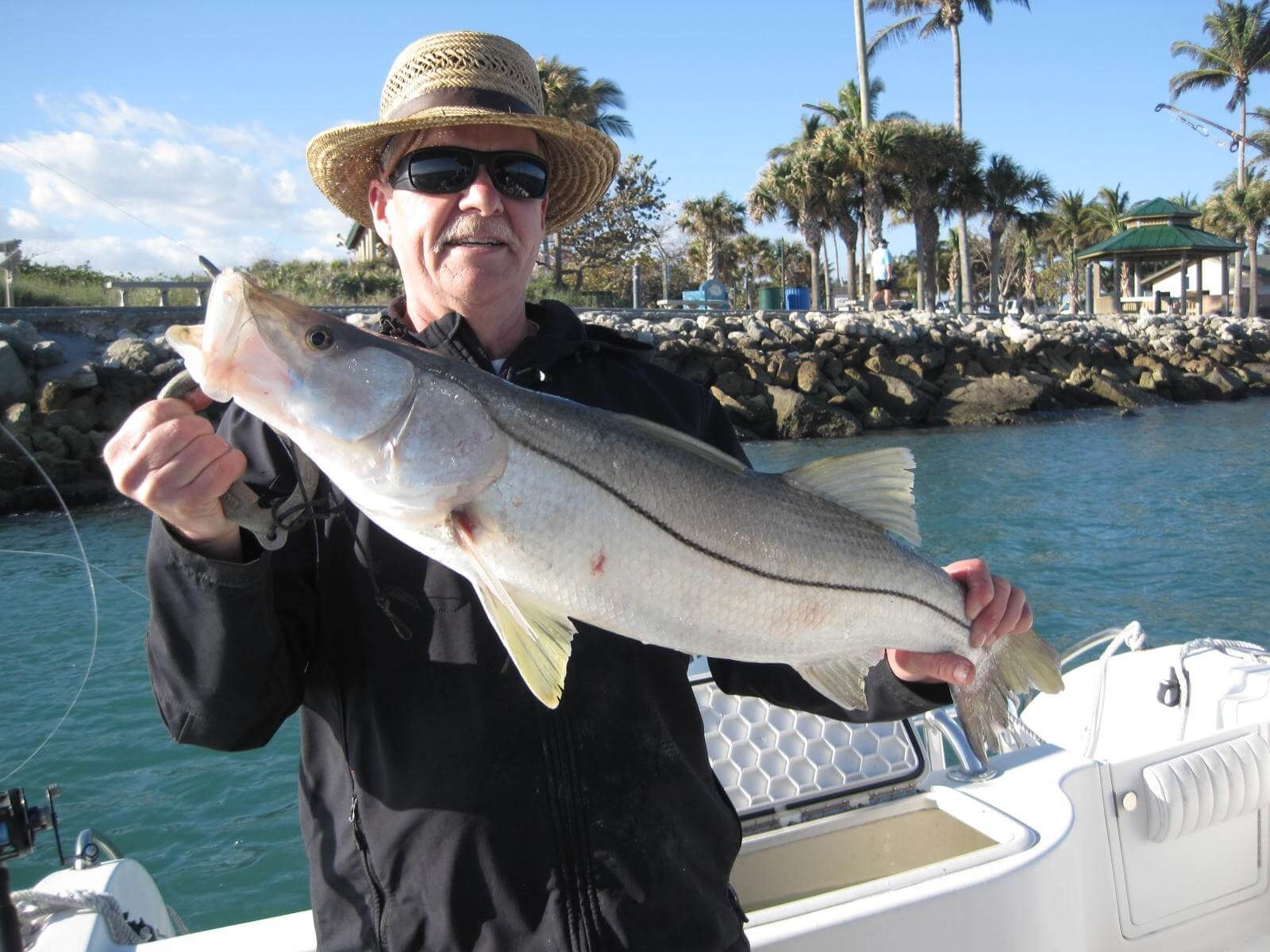 A man in a straw hat is holding a large fish in his hands.