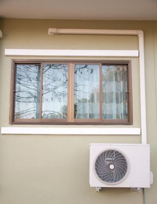 Window with brown frame and wall-mounted air conditioner on a beige building exterior