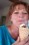 A woman in a blue shirt is eating an ice cream cone.