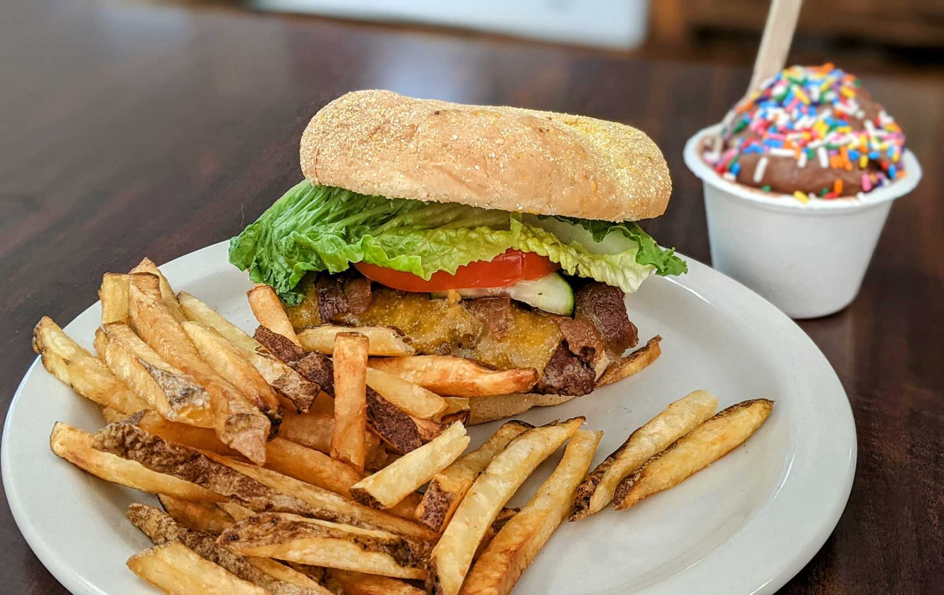 A hamburger and french fries on a plate next to a cup of ice cream.
