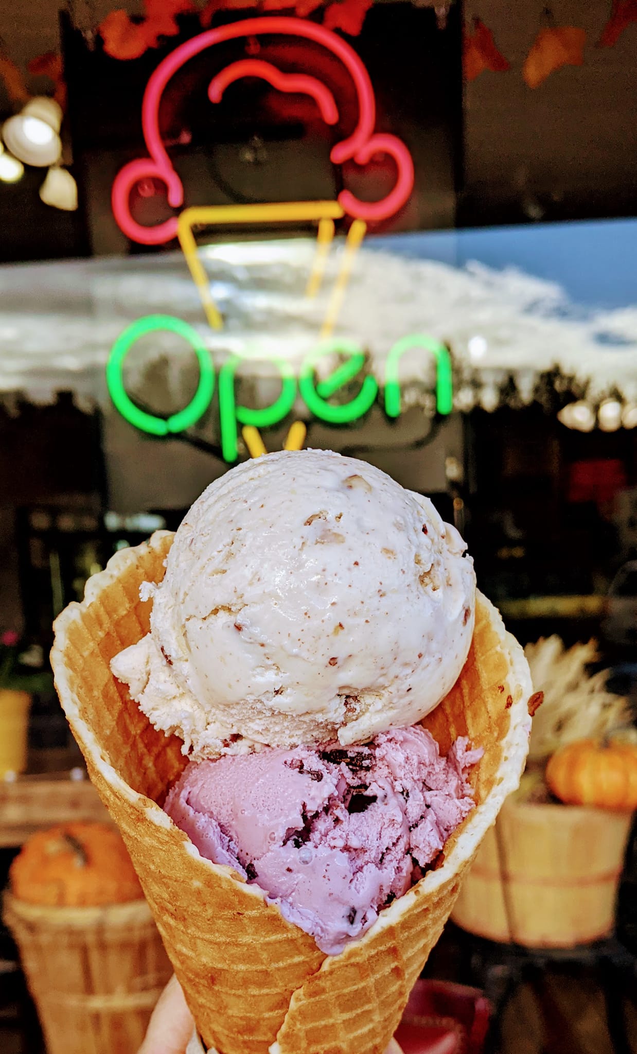 A person is holding a cone of ice cream in front of an open sign.