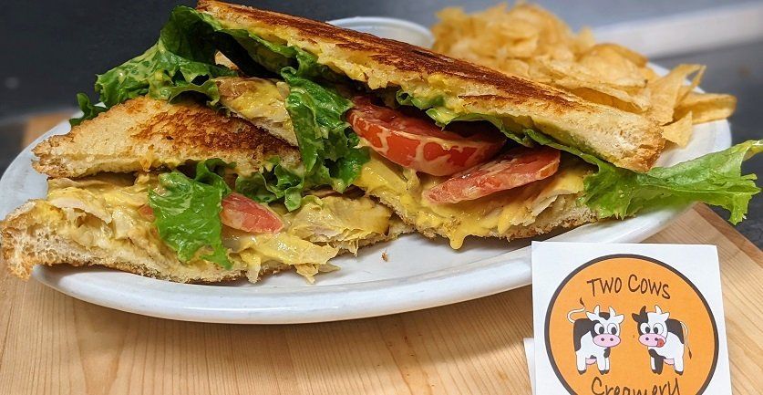 A grilled cheese sandwich with lettuce and tomatoes on a plate with chips.