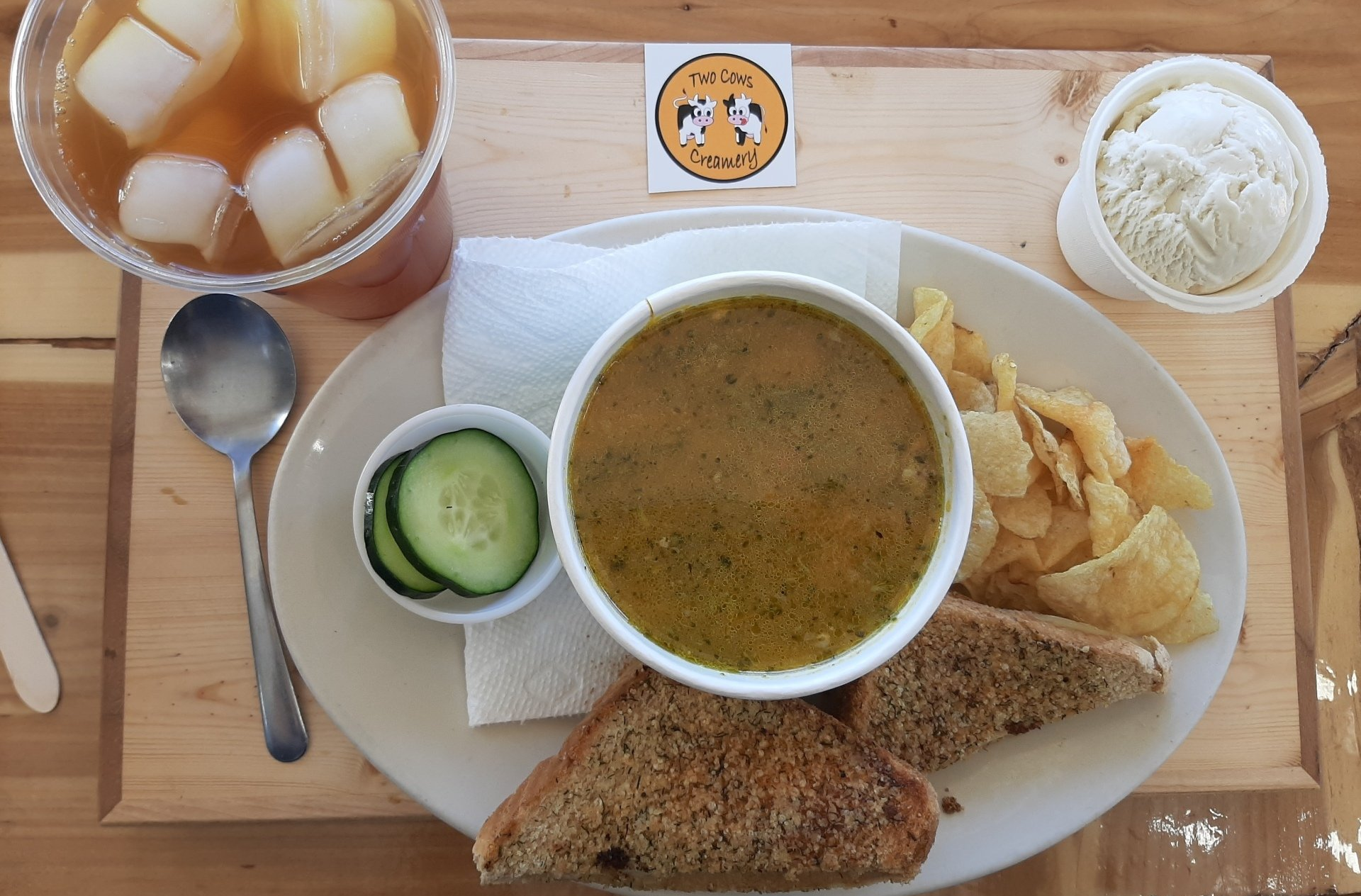A plate of food with a bowl of soup , sandwich , chips and iced tea.