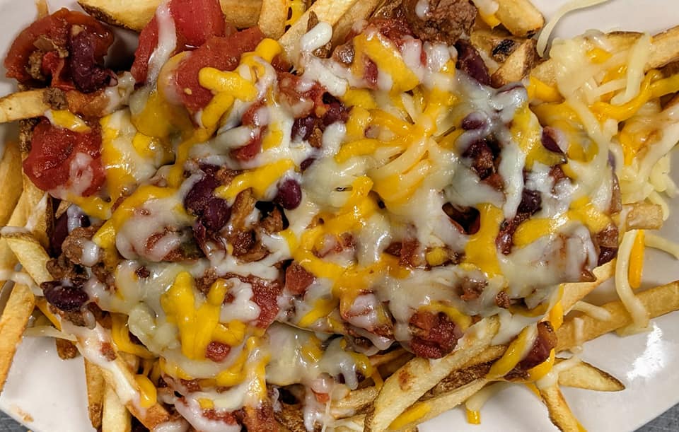 A white plate topped with french fries , chili , cheese and beans.