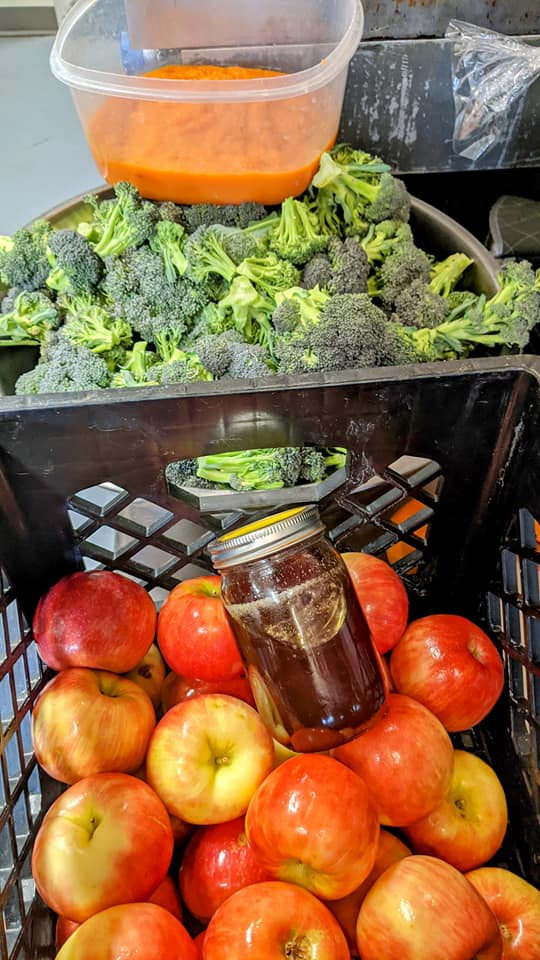 A crate filled with apples , broccoli and a jar of honey.