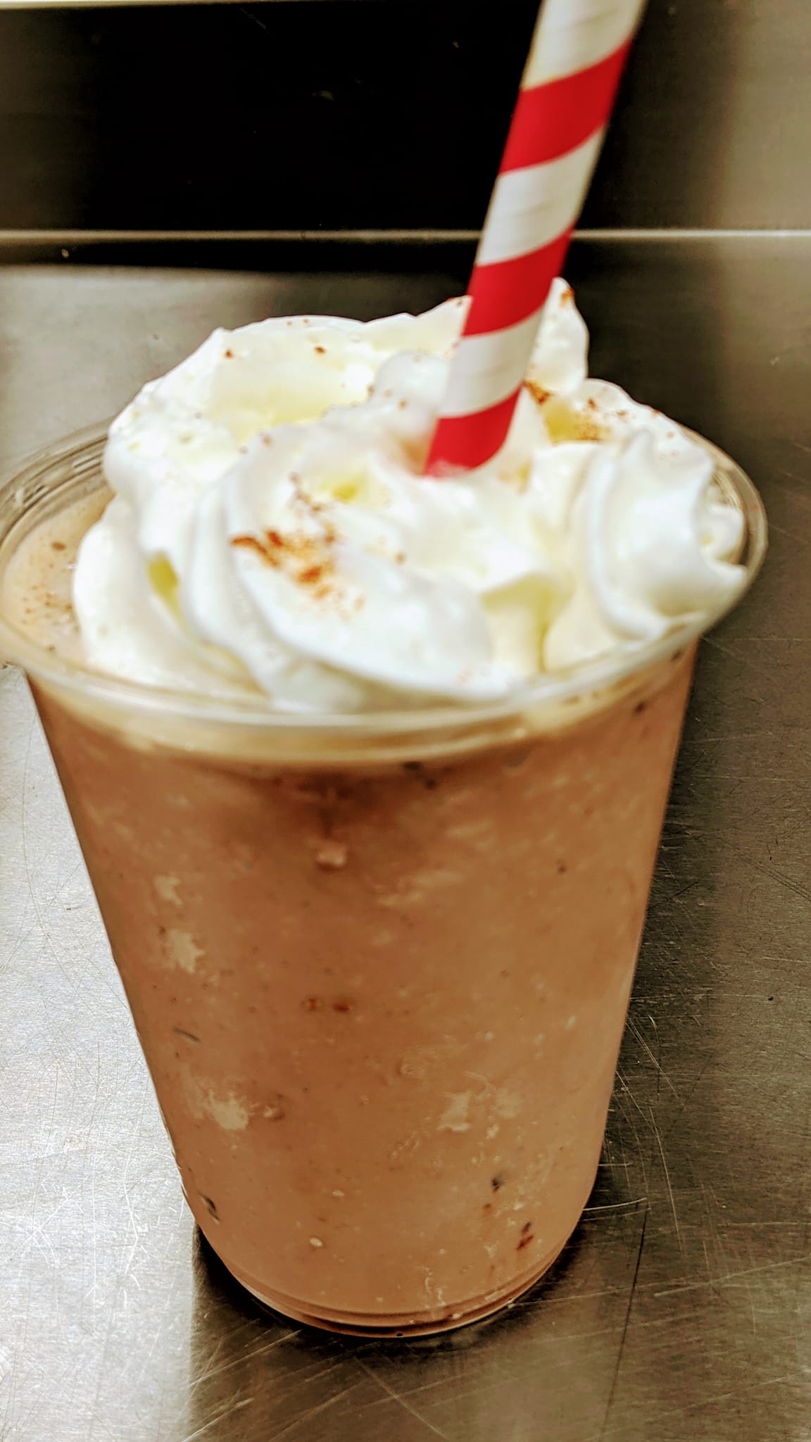 A close up of a milkshake with whipped cream and a straw on a table.