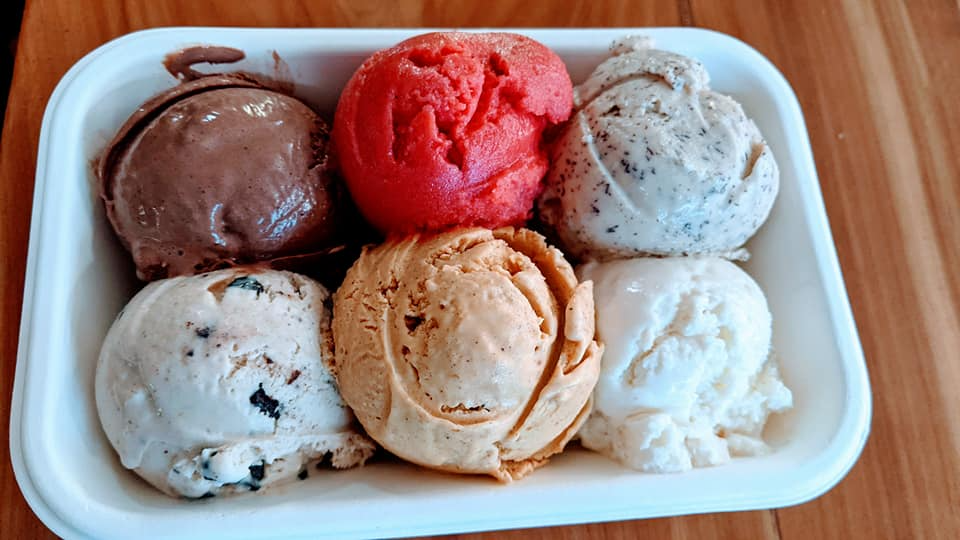 A tray of ice cream scoops of different flavors on a wooden table.