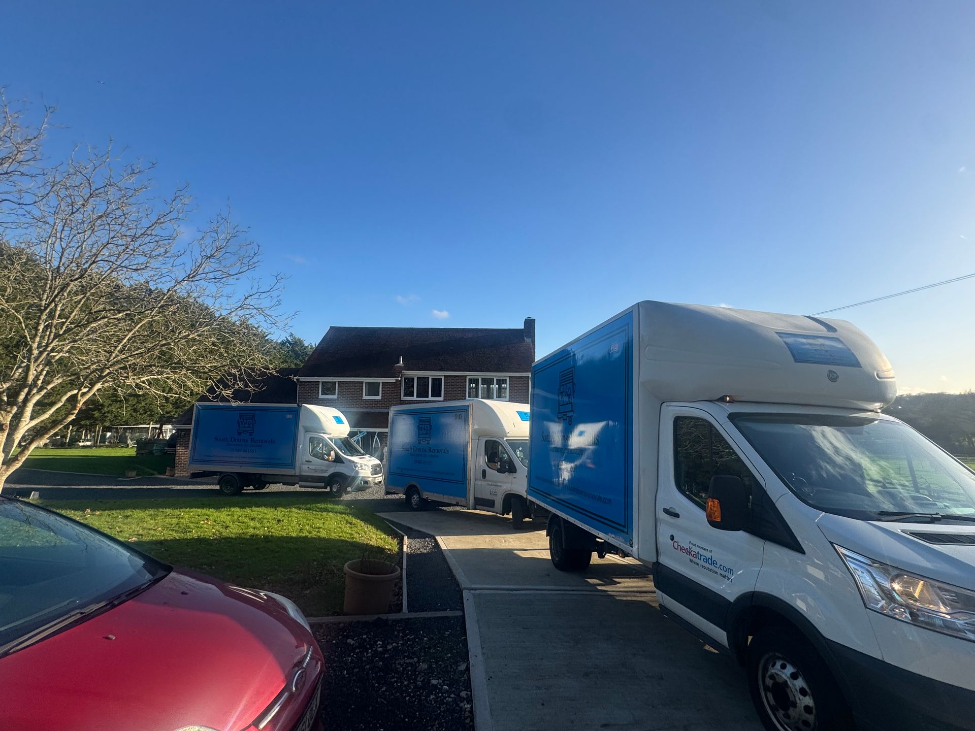 Several white and blue moving trucks parked in front of a house on a sunny day.