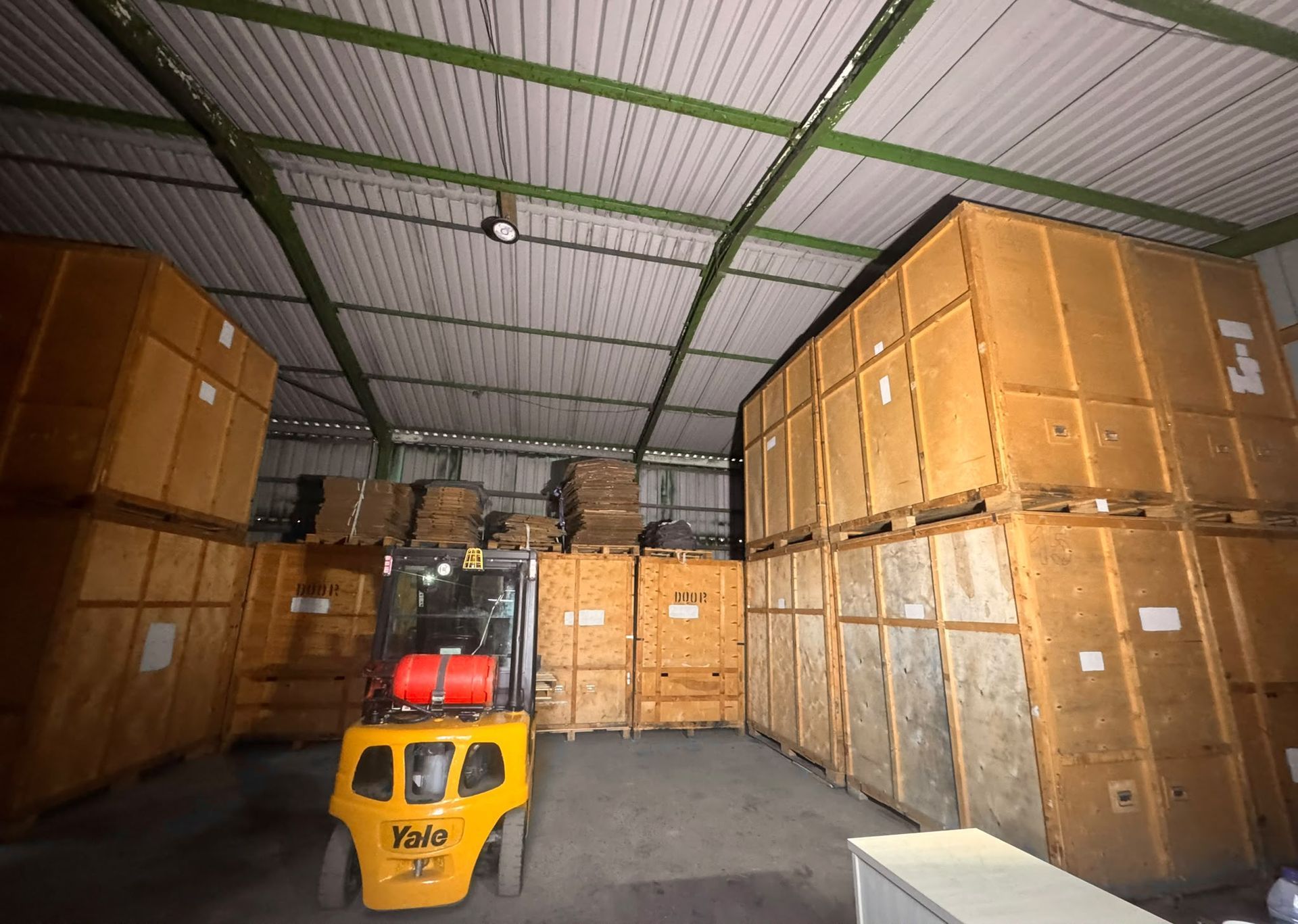 Warehouse aisle with stacked wooden crates and a yellow pallet jack in the foreground