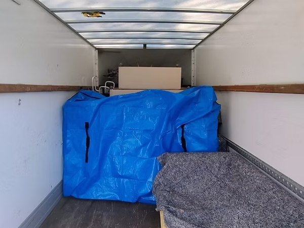 Interior of a moving truck with a blue tarp-covered item and a gray blanket on a wooden bench.