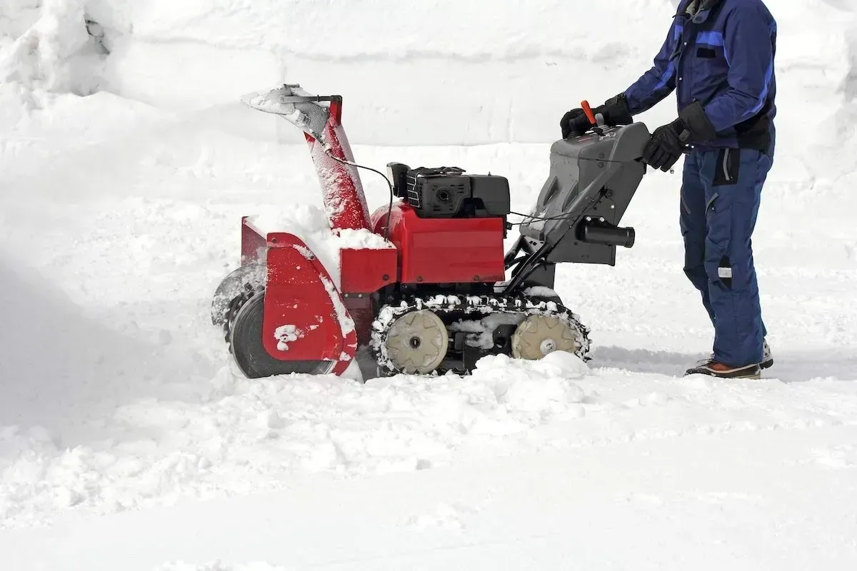 Red snowblower clearing deep snow, operated by a person in blue winter clothes.