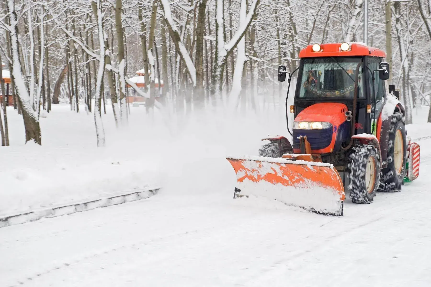 Orange snowplow clearing a snowy road in a winter forest