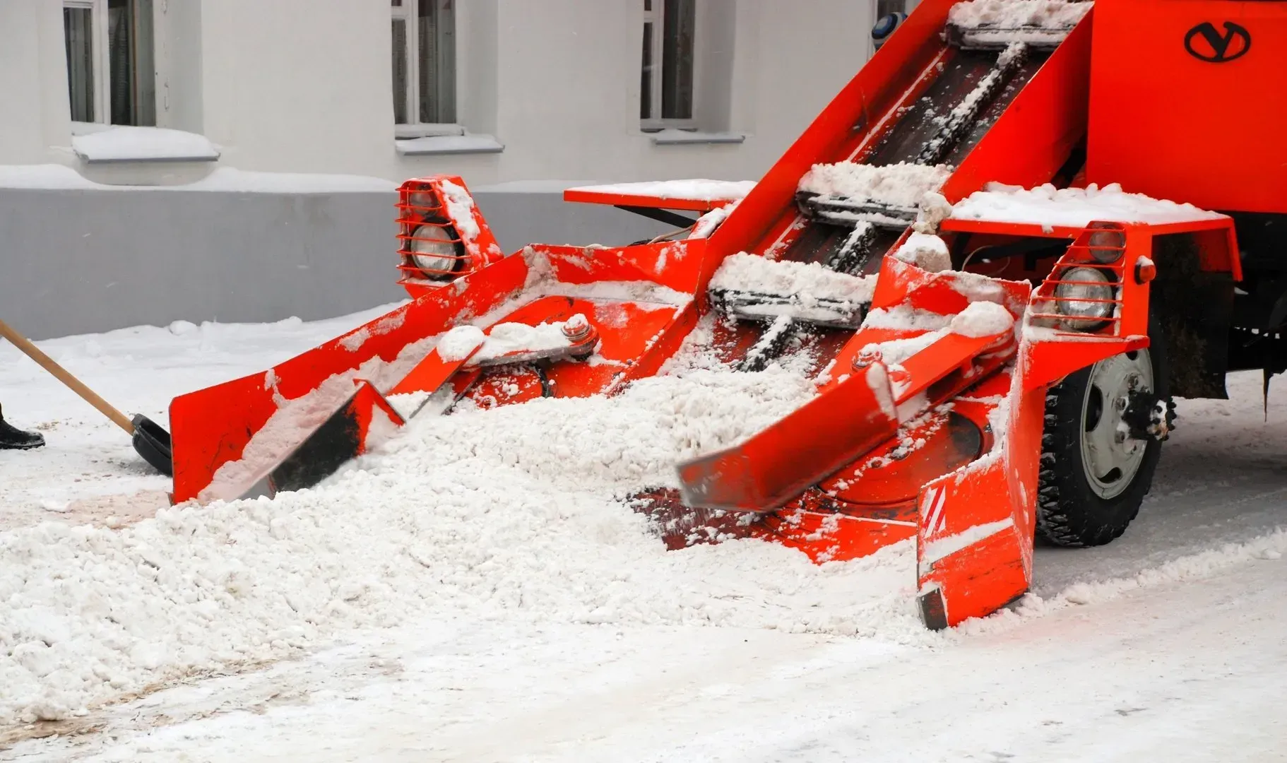 Red snowplow clearing snow on a street beside a building