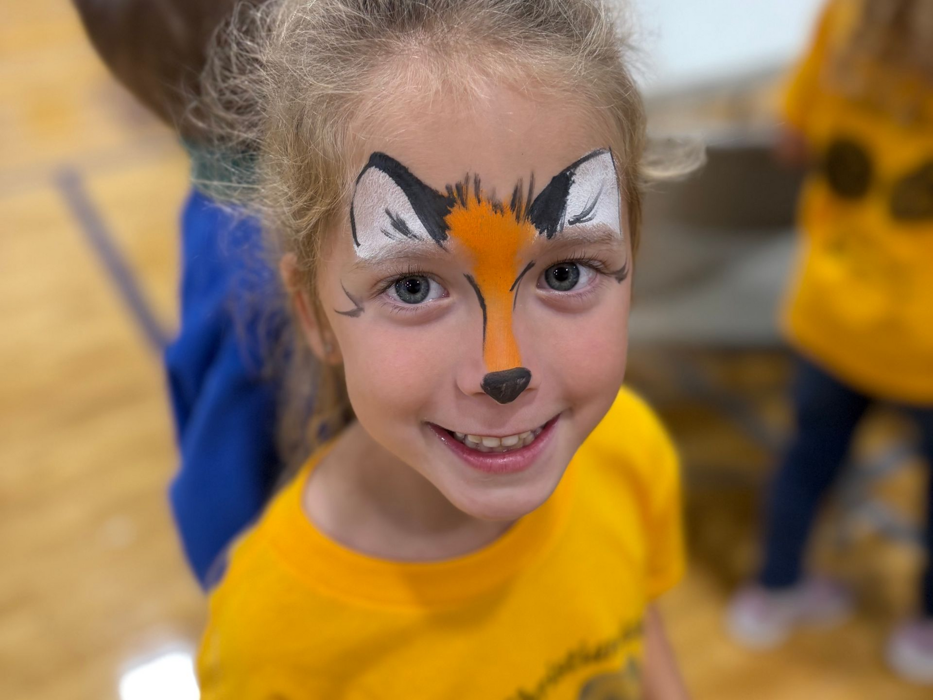 Child with fox face paint smiling in a yellow shirt indoors