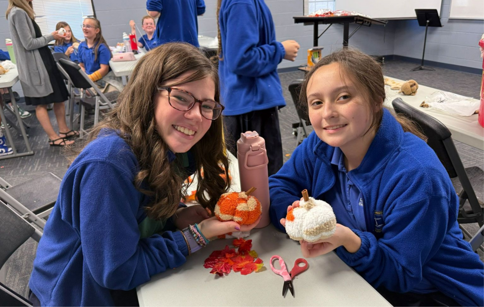 Two girls in blue hoodies smiling at a table with desserts and red decorations.