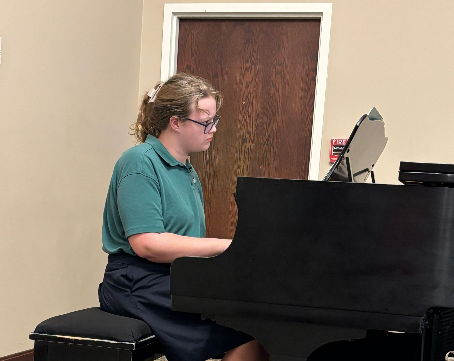 Person in a green shirt playing a black piano in a room.