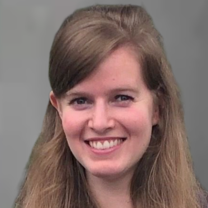 Smiling person with curly hair in front of a gray backdrop