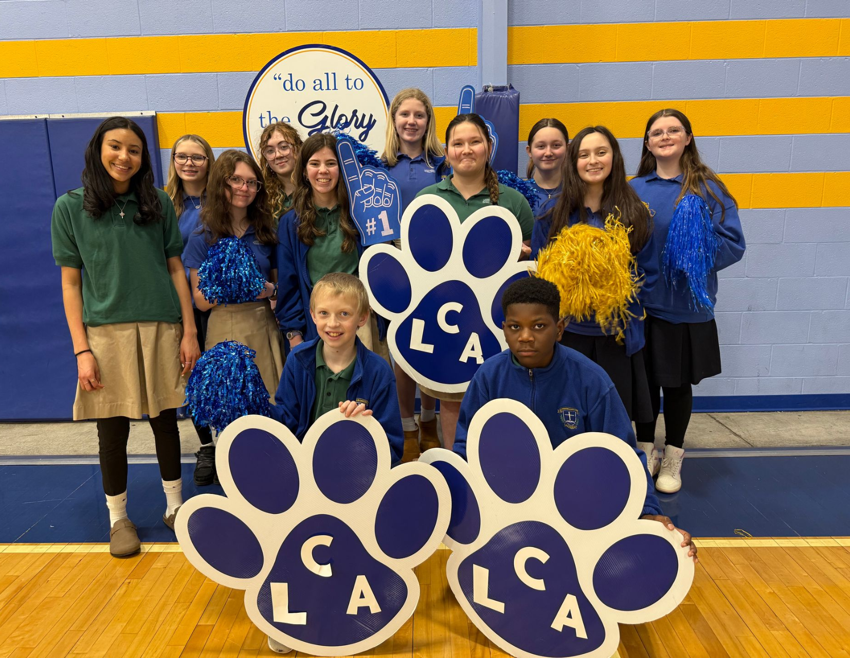 Group posing in a gym with large blue paw-print CLA signs and blue-and-gold team outfits.