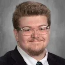 Portrait of a smiling person with glasses and dark wavy hair against a gray background