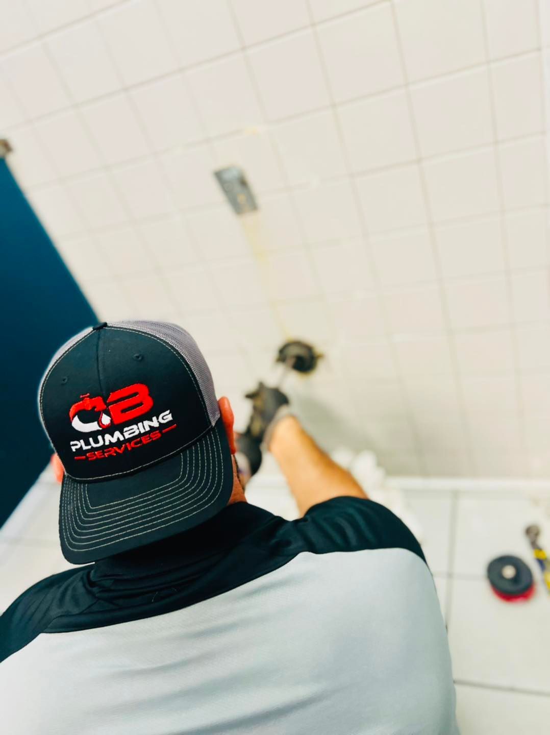 a plumber wearing a hat that says cb plumbing services on it while fixing faucet
