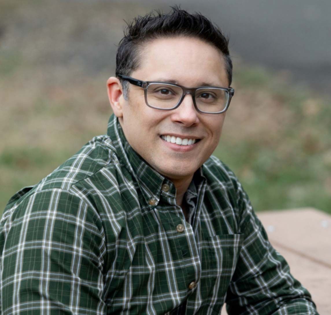 A man wearing glasses and a plaid shirt smiles for the camera