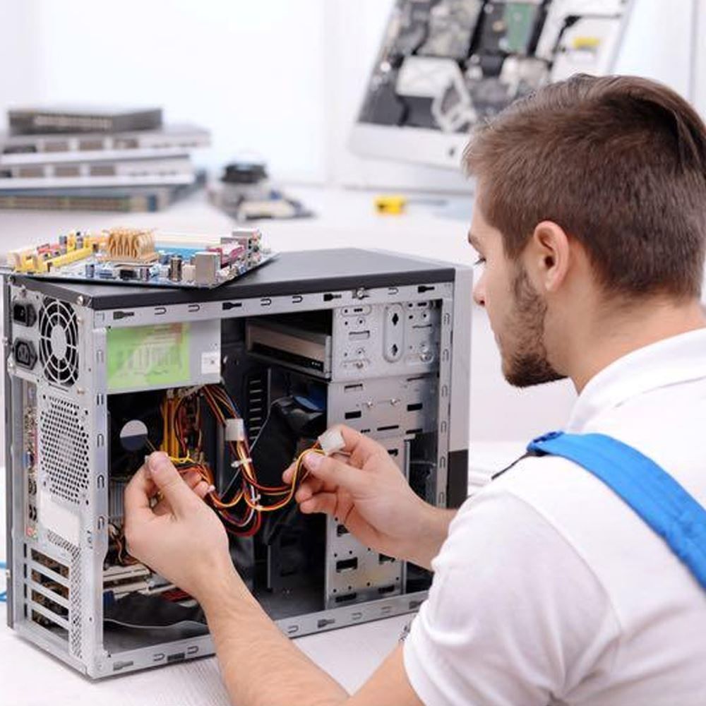Technician wiring an open desktop computer on a workbench, with tools and components nearby