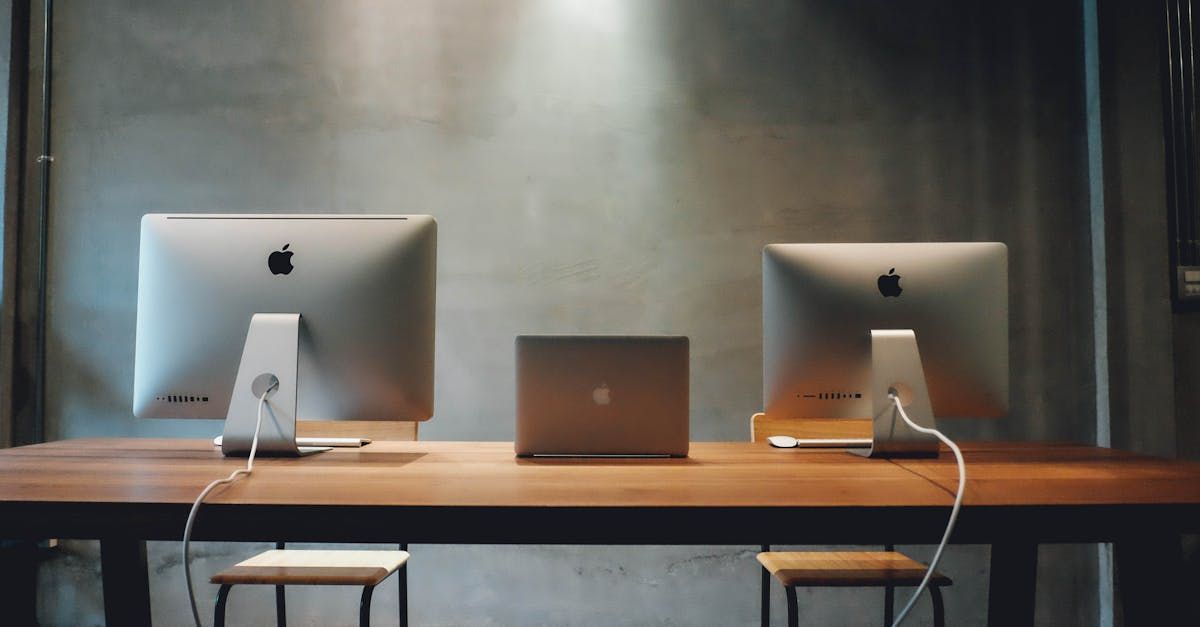 Two computer monitors and a laptop are sitting on a wooden table.