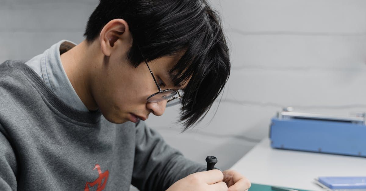 A young man wearing glasses is sitting at a table holding a chess piece.
