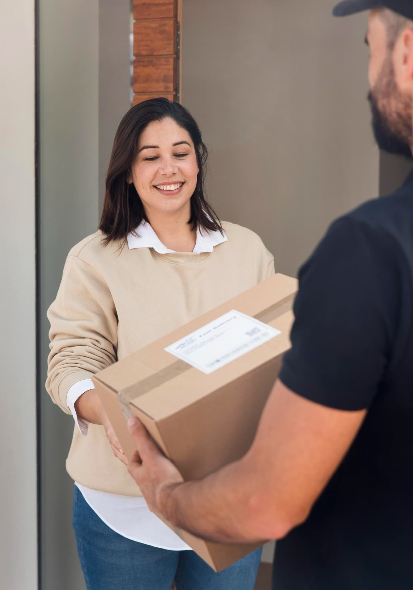 Entregador entregando um pacote de papelão a um cliente sorridente na porta de casa.