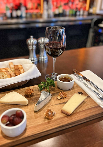 Cheese board with wine, bread, grapes, and nuts on a wooden table.