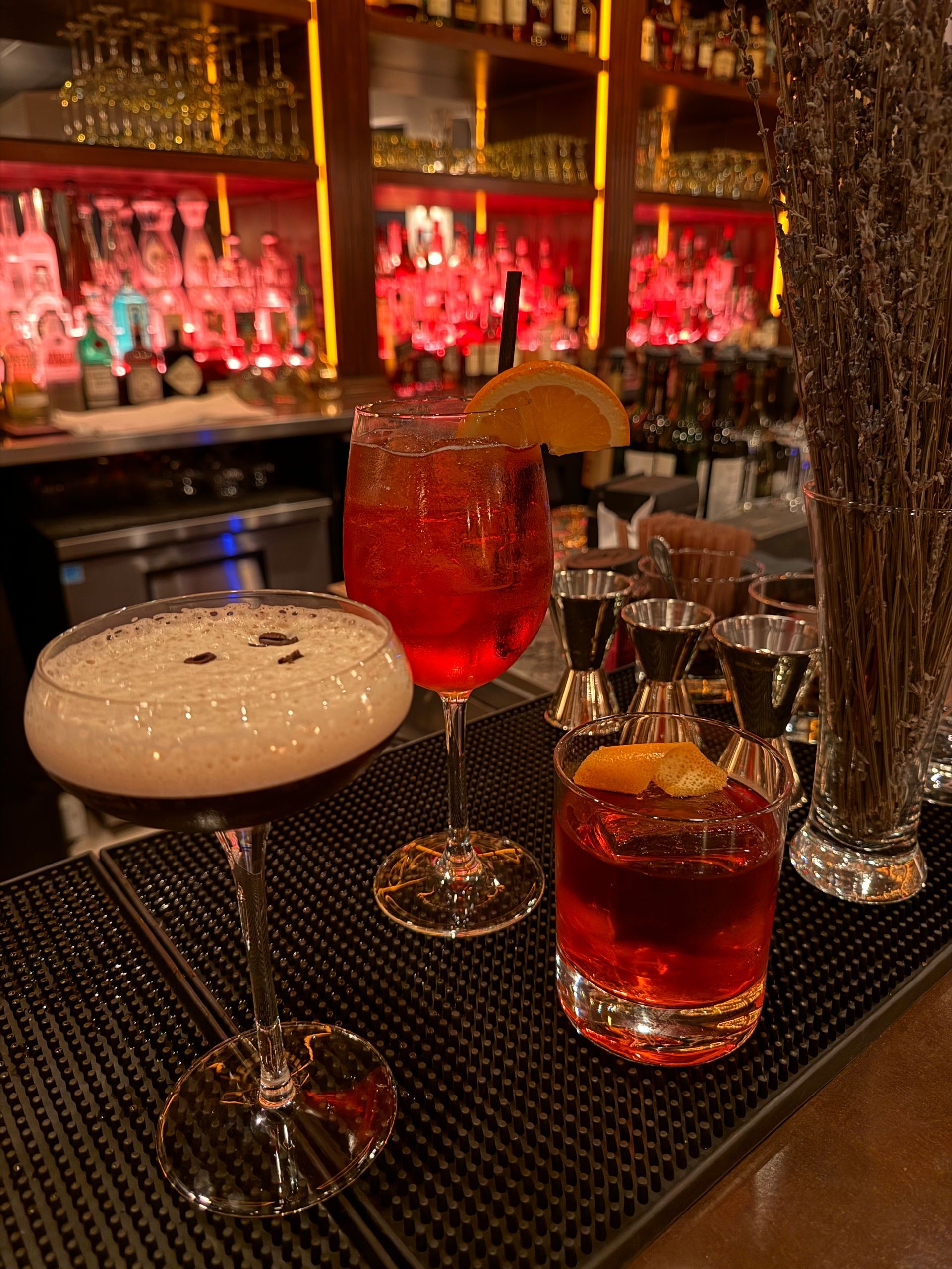 Three cocktails on a bar counter with a dim, red-lit background.