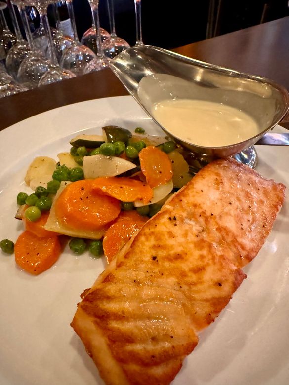 Grilled salmon with vegetables and creamy sauce on a white plate.