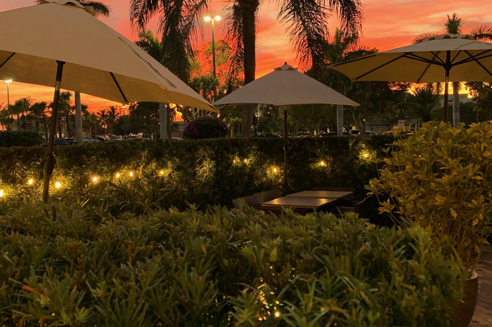 Outdoor dining area at sunset with yellow umbrellas, glowing lights, and orange sky.