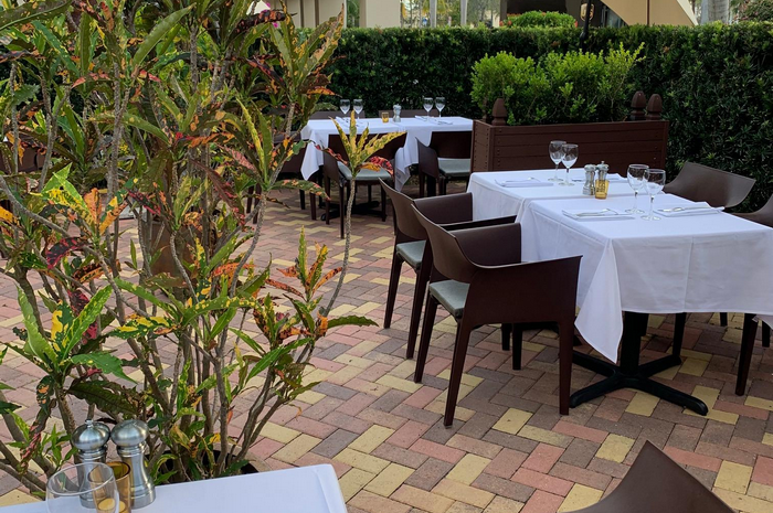 Outdoor restaurant seating with white tablecloths and modern chairs, surrounded by greenery.