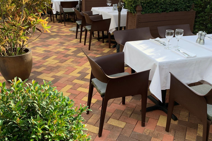 Outdoor dining area with tables set for service on a brick patio.