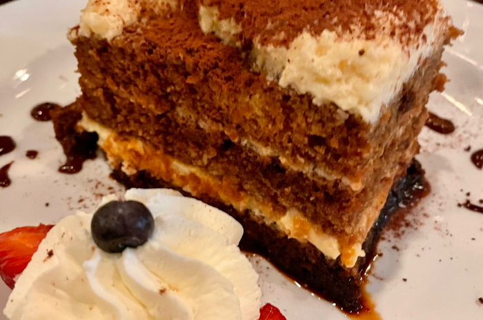 Tiramisu slice with whipped cream and berries on a white plate.
