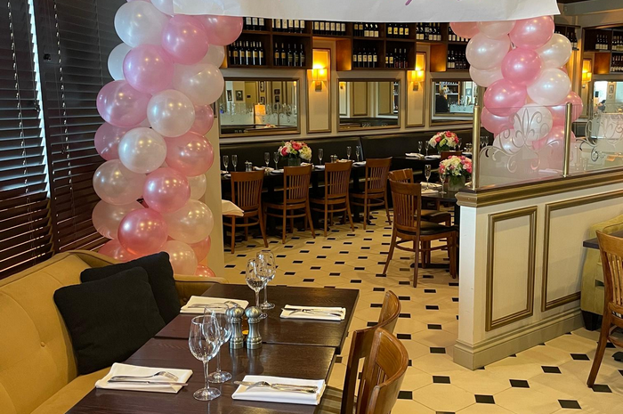 Restaurant interior decorated with pink and white balloons; tables set for a party.